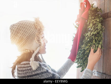Vista laterale della giovane donna appeso ghirlanda di Natale sulla porta di ingresso Foto Stock