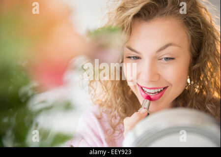 Giovane donna applicando un rossetto rosso nella parte anteriore dello specchio Foto Stock