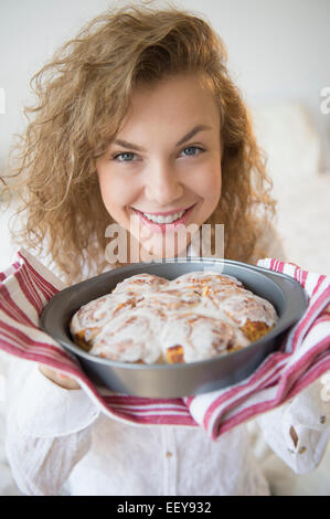 Ritratto di giovane sorridente donna che mantiene freschi panini alla cannella Foto Stock