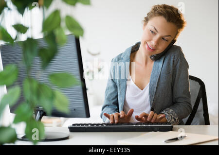 Giovane imprenditrice lavorando sul computer desktop in ufficio Foto Stock