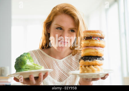 Giovane donna tenendo la piastra con ciambelle e con broccoli Foto Stock
