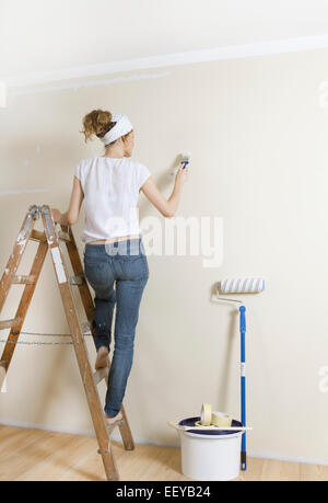 Giovane donna in piedi su una scaletta e pittura un muro nuovo Foto Stock