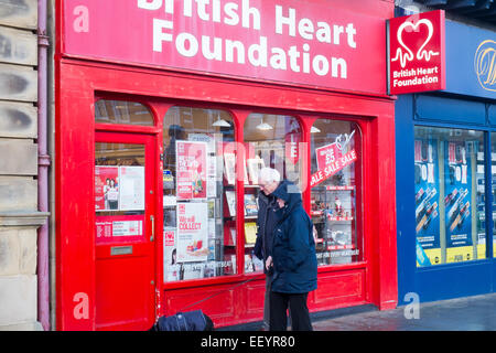 Coppia di anziani a piedi il loro cane passato British Heart Foundation shop a Lytham St Annes, Lancashire, Inghilterra Foto Stock