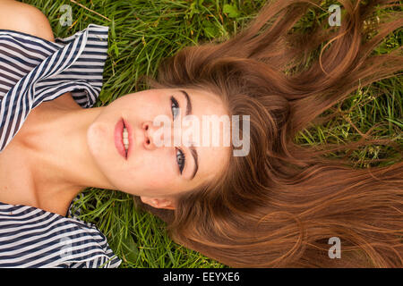 Piuttosto giovane con i capelli lunghi ragazza distesa sul verde del prato, close-up. Foto Stock