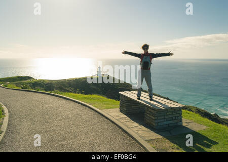 Il faro di Cape Reinga nel lontano nord, Nuova Zelanda. Uno stand turistico su un banco di lavoro con le braccia tese. Retroilluminazione. Foto Stock