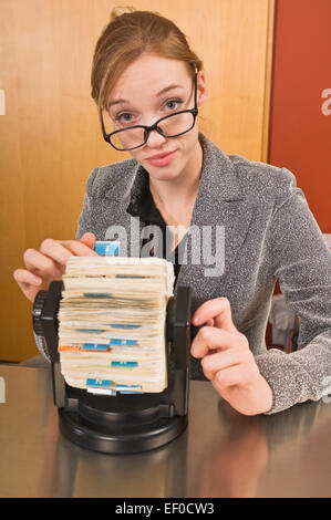 Office receptionist guardando attraverso il Rotary rubrica indirizzi Foto Stock