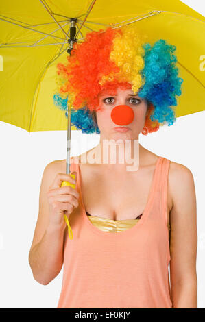 Donna che indossa un clown parrucca e azienda Ombrello giallo Foto Stock