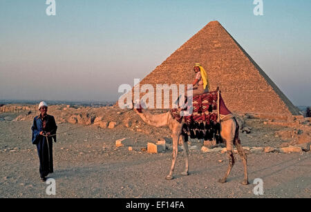 Un turista femminile a dorso di un cammello in posa per una foto in 1999 come il sole tramonta una delle antiche piramidi a Giza sulla periferia del Cairo, Egitto. Quasi15 milioni di turisti hanno visitato questo Nord nazione africana nell'anno antecedente alla rivoluzione egiziana del 2011, che ha ridotto il numero da 45% a causa di successivi tumulti nel paese. Foto Stock