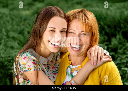 Madre con sua figlia sorridente e abbracciando vestito in giallo nel parco Foto Stock