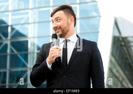 Toastmaster o newsmaker posa con microfono su sfondo contempopary Foto Stock