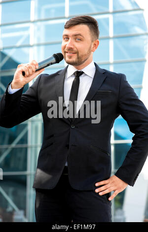 Toastmaster o newsmaker posa con microfono su sfondo contempopary Foto Stock