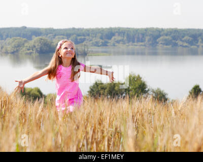 Felice ragazza nel campo estivo vicino al lago in una giornata di sole Foto Stock