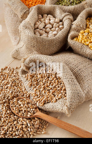 Borsa di Hesse con frumento e il cucchiaio di legno closeup; piselli, ceci, lenticchie rosse nel sacco e mung verde sullo sfondo Foto Stock