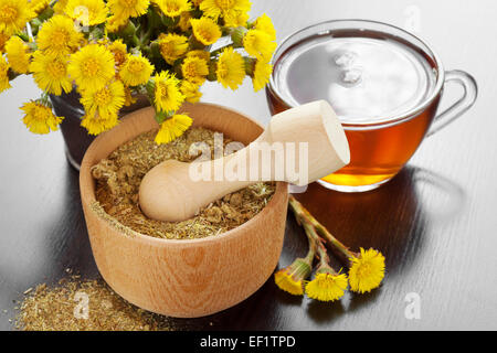 Mortaio e pestello, salutare tè e secchio con i fiori coltsfoot, medicine a base di erbe Foto Stock