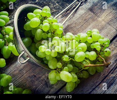 Le uve in metallo scolapasta su legno tavolo rustico, vintage stilizzata Foto Stock