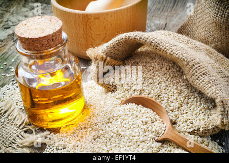 Semi di sesamo nel sacco e bottiglia di olio su legno tavolo rustico Foto Stock