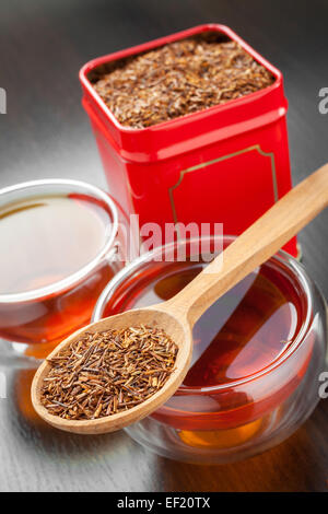Rooibos in cucchiaio di legno, due tazze di tè e tè la scatola di stagno su tavola Foto Stock