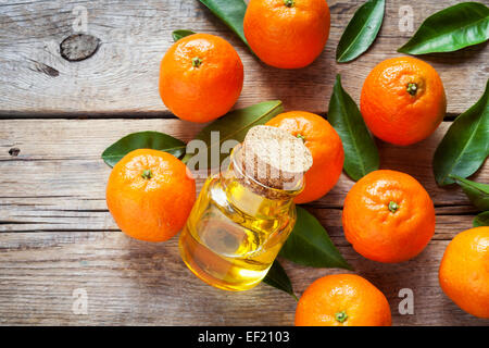 Mature tangerini con foglie e bottiglia di elementi essenziali di agrumi Olio su di un tavolo di legno. Foto Stock