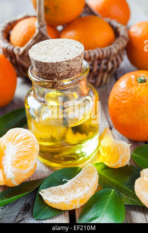 Bottiglia di essenziale di olio di agrumi e mature, tangerini nel cesto su legno vecchio tavolo da cucina. Foto Stock