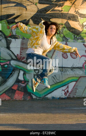 Ragazza adolescente saltando di fronte coperto di graffiti wall Foto Stock