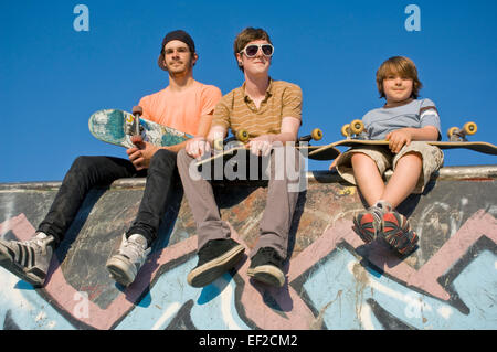 Tre giovani uomini seduti su una parete in corrispondenza di uno skatepark Foto Stock