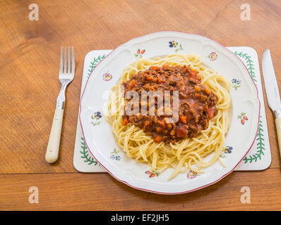 Una piastra con una grande porzione di deliziose cotte in casa spaghetti alla bolognese servita su un fiorito di porcellana bianca piastra su una tavola di legno Foto Stock