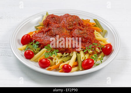 Cucinata fresca pasta di penne polpette fatte in casa, pomodorini e prezzemolo sulla piastra bianca con tavolo bianco come sfondo. Foto Stock