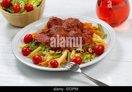 Pasta fresca, polpette di carne in salsa densa, pomodori ciliegini, prezzemolo, vino rosso e insalata con legno di colore bianco al di sotto. Foto Stock