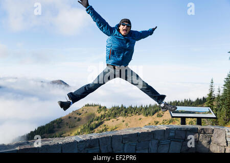 Giovane maschio saltare direttamente su di una parete, con le sue gambe si diffondono in un divertente pongono, con un bellissimo sfondo di montagna Foto Stock