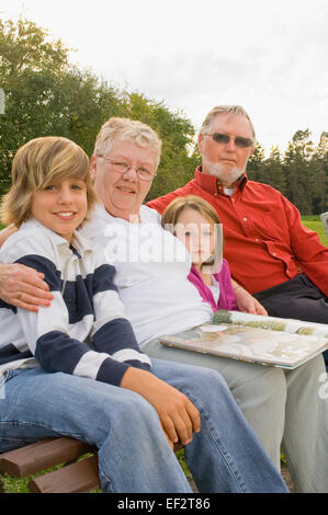 Nonni e nipoti seduti su una panchina nel parco Foto Stock