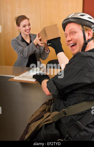 Corriere bicicletta dando al box office receptionist Foto Stock