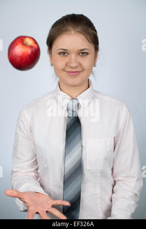 Azienda giovane donna che indossa camicia e cravatta gioca con la mela rossa Foto Stock