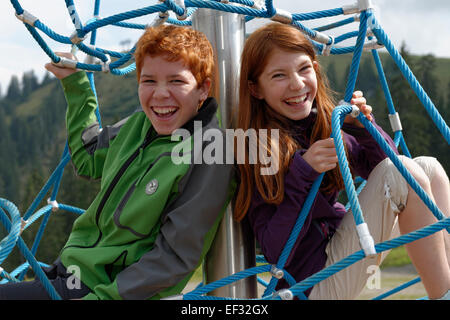 Fratelli, bambini seduti in un telaio di arrampicata presso il parco giochi a Jagahüttn auf der Sutten, Tegernsee Montagne Foto Stock