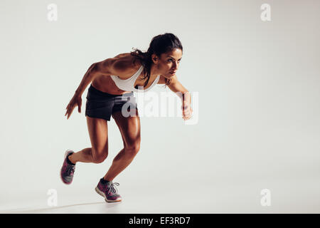 Energico giovane donna in esecuzione su sfondo grigio. Focalizzato giovane atleta femminile in esecuzione. Foto Stock