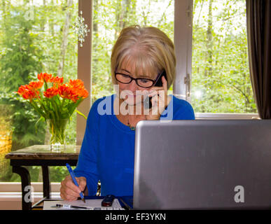 Coppia donna più anziana a lavorare con il computer portatile e i file e telefono in ufficio a casa. Vaso di fiori sulla tavola in background. Foto Stock