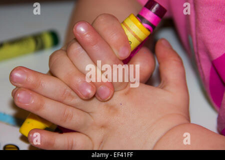 Giovane ragazza che gioca con le matite colorate nelle sue mani. Foto Stock