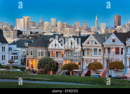 L'iconico "Painted Ladies' con il centro cittadino di San Francisco Skyline dietro fotografato dopo il tramonto da Alamo Square a San Francisco, California. Foto Stock