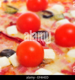 Primo piano di una pizza con pancetta, olive, pomodori ciliegini, formaggio di capra, peperone verde e melanzane Foto Stock