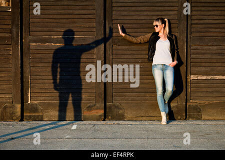 Giovane donna gesticolando con silhouette di un giovane uomo contro la parete in legno Foto Stock