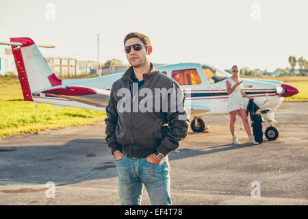 Giovane uomo su airfield, donna in aereo in background Foto Stock