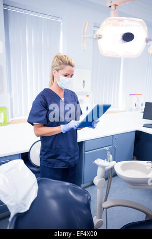 Dentista in maschera e scrub blu utilizzando il suo tablet Foto Stock