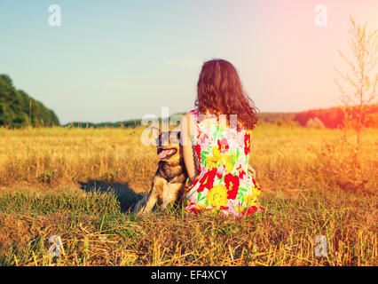 Giovane donna con il cane nel campo alla luce del tramonto torna alla fotocamera Foto Stock