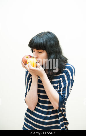 Bruna ragazza in abiti casual odori apple e orange nelle sue mani su sfondo bianco Foto Stock