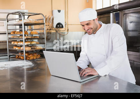 Sorridente baker utilizzando laptop sul piano di lavoro Foto Stock