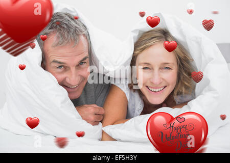 Immagine composita di felice coppia di mezza età sotto il piumino Foto Stock