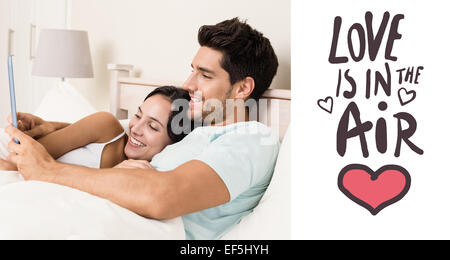 Immagine composita della coppia attraente che giace nel letto con i tablet pc Foto Stock
