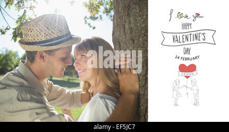 Immagine composita di carino coppia sorridente appoggiata contro la struttura ad albero nel parco Foto Stock