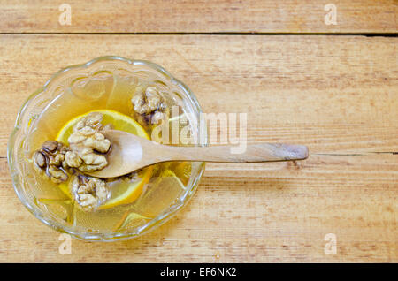 Piatto piccolo riempito con il miele, le fette di limone e le noci su di un tavolo di legno Foto Stock