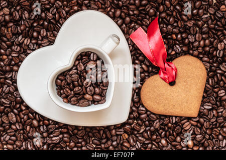 Caffè il concetto di tempo. Cuore di coppa a forma di piastra e cookie gingerbread su i chicchi di caffè sfondo. Vista superiore Foto Stock