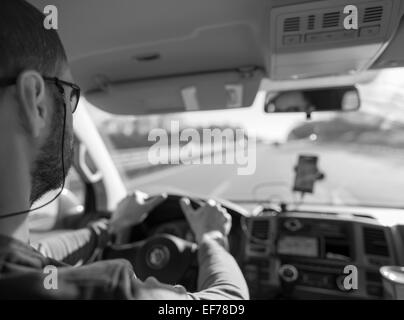 In bianco e nero girato di un uomo dietro la ruota, alla guida di auto in autostrada. Foto Stock